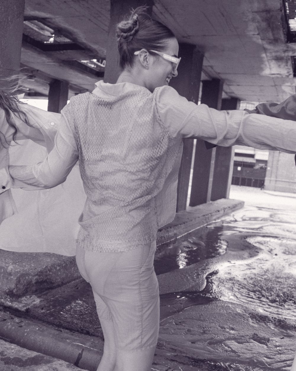 A woman in a sheer shirt dancing with friends through a flooded underpass