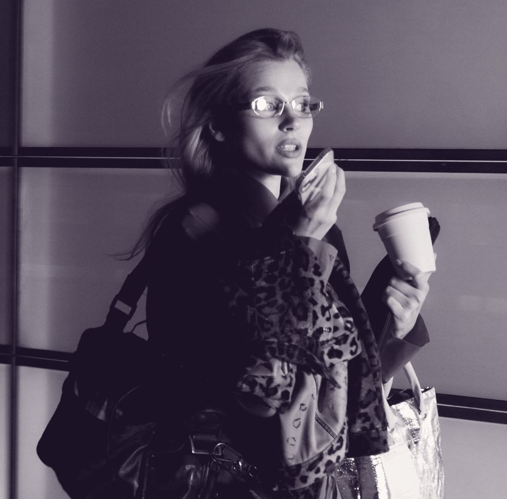 A woman in a leopard coat walking with a coffee, mid-sentence