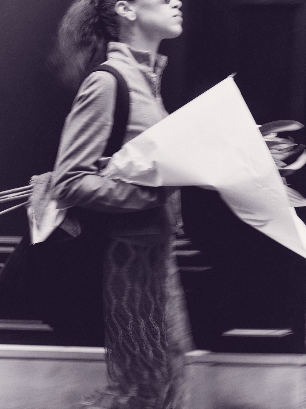 A woman walking down a city street carrying flowers wrapped in paper