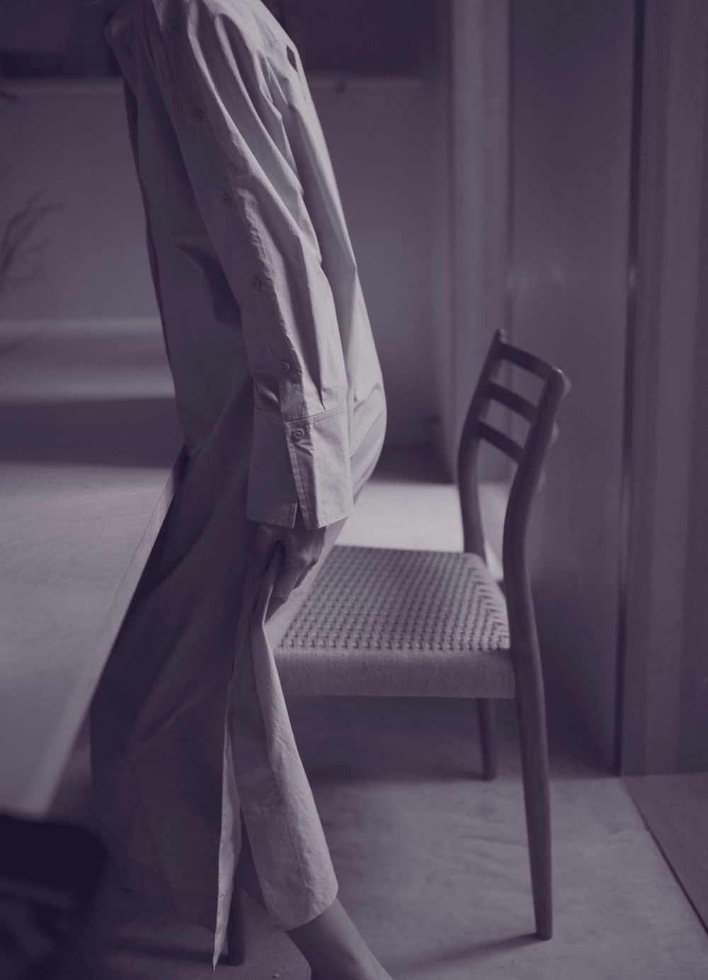 A woman in a long linen shirt dress rising from a wooden chair