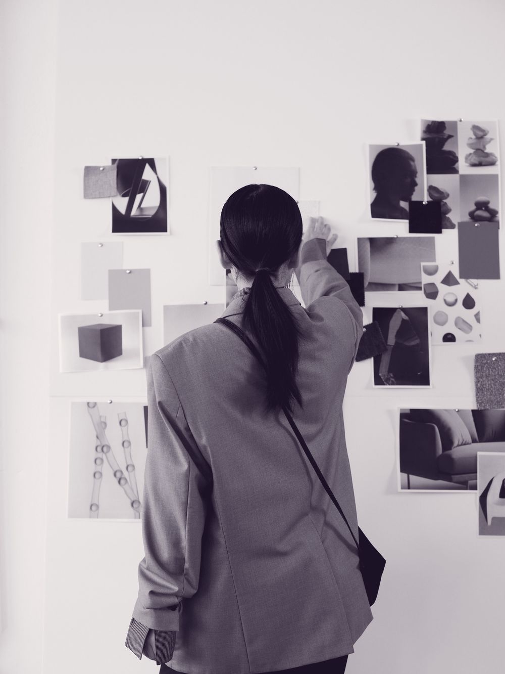 A woman in a blazer pinning photographs to a studio wall