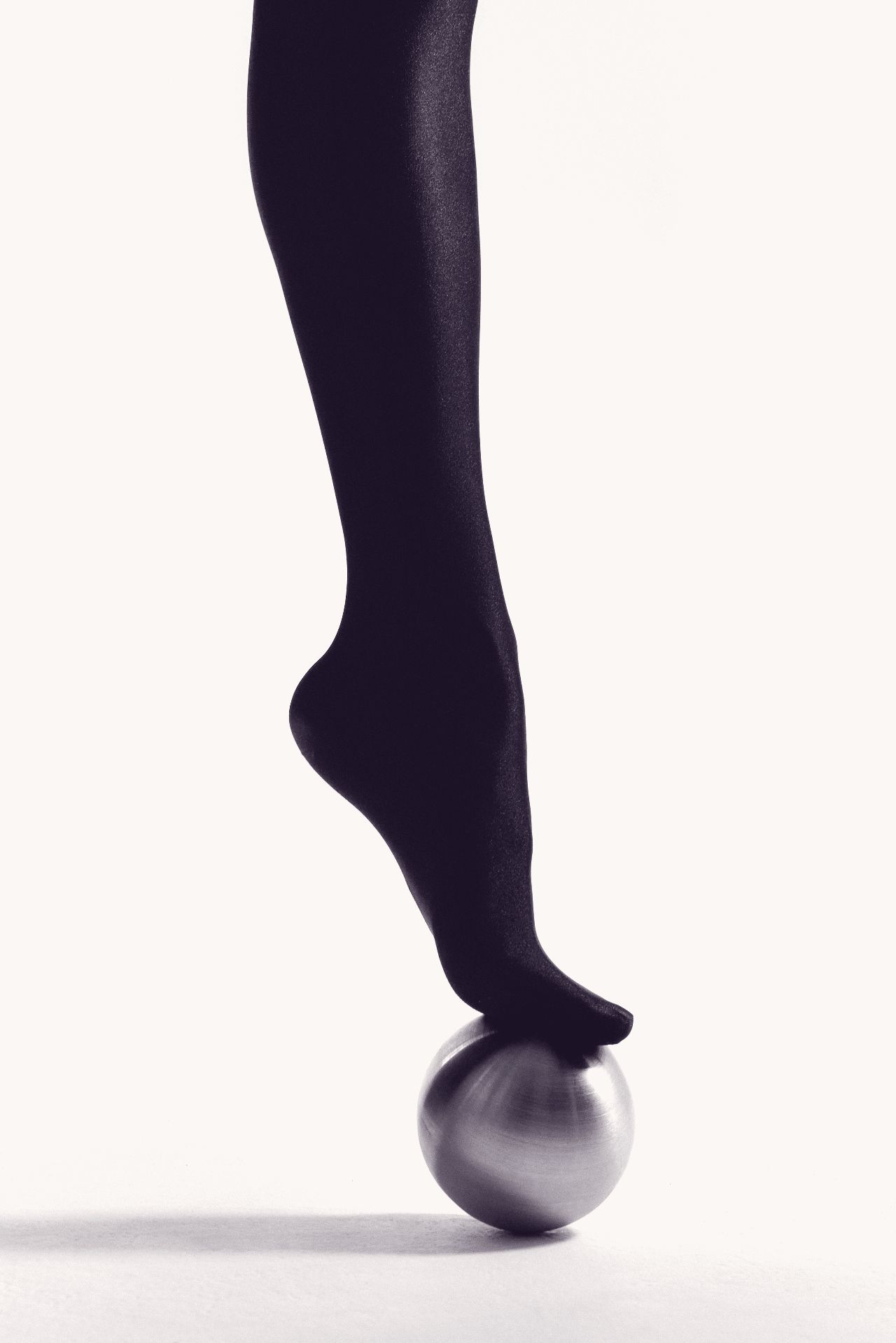 A foot in dark tights balanced on its toes on a polished steel sphere